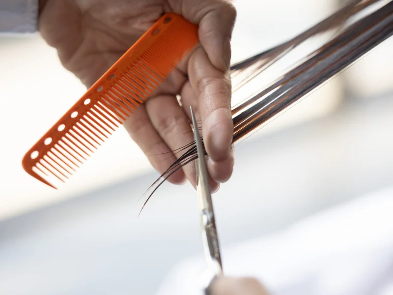 Primo piano di forbici professionali da parrucchiere e pettine appoggiati su una superficie scura, simboleggianti la precisione tecnica necessaria per creare la firma stilistica di un salone.